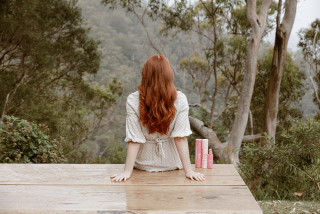Person with red hair sitting at a wooden table overlooking a forest